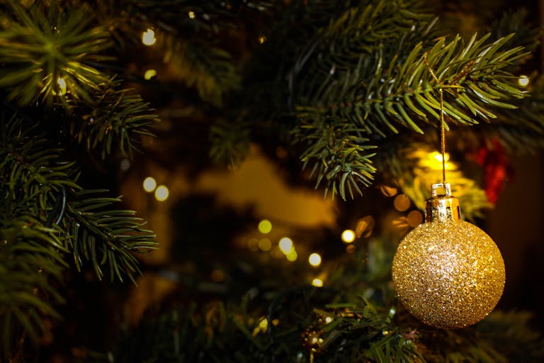 A sparkling gold ornament hanging on a lush Christmas tree, adorned with festive lights.